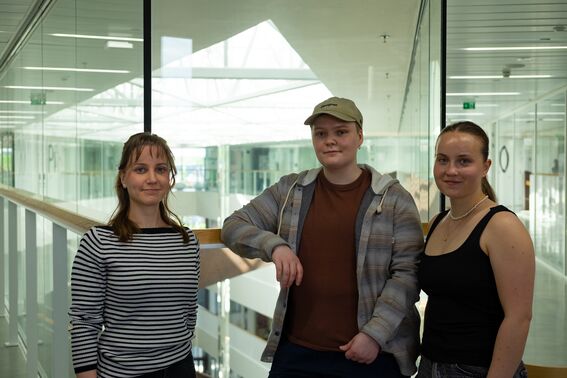 Design students Taija Piikkilä, Kasi Jutila and Leena Hurtig stand in a bright modern corridor with glass walls at the School of Arts, Design and Architecture.
