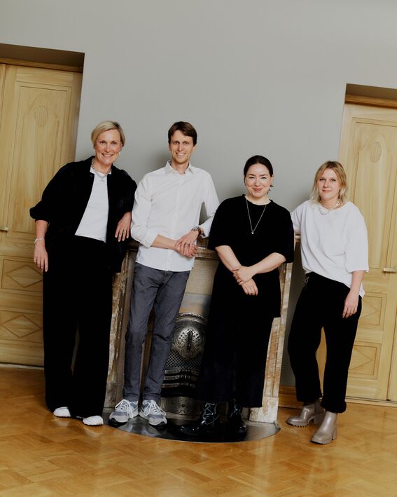Monika Nars, Konrad Klockars, Noora Yau ja Anna Semi seisovat takan edessä valoisassa huoneessa, jossa puiset ovet ja parkettilattia