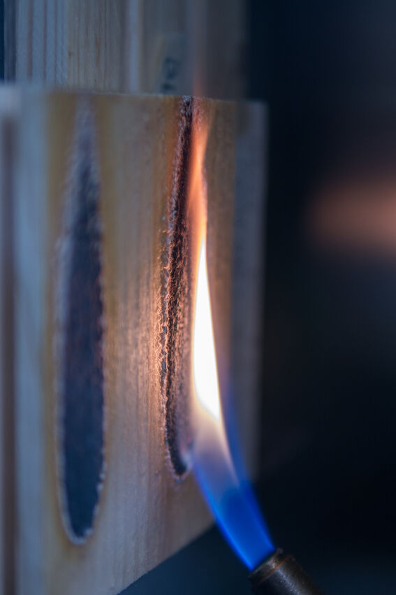 Blue gas flame burning a vertical groove in a light wooden block during a close-up fire test.
