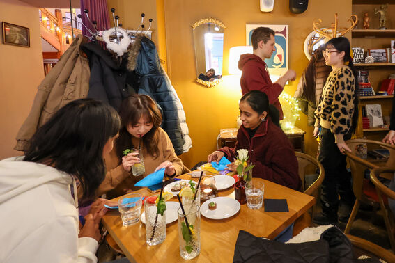 Group of young people in a cosy café, chatting around a wooden table with drinks and snacks