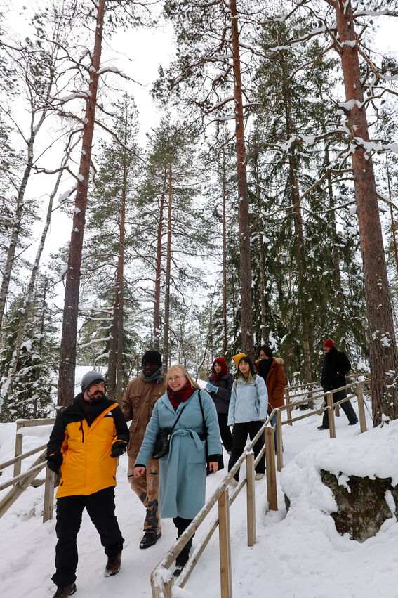Smiling group walks down a snowy forest path with tall pine trees and wooden railings