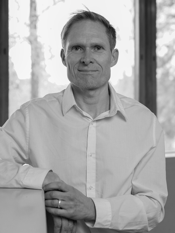 Man in light shirt leaning on a surface indoors, black and white portrait, trees visible through windows behind