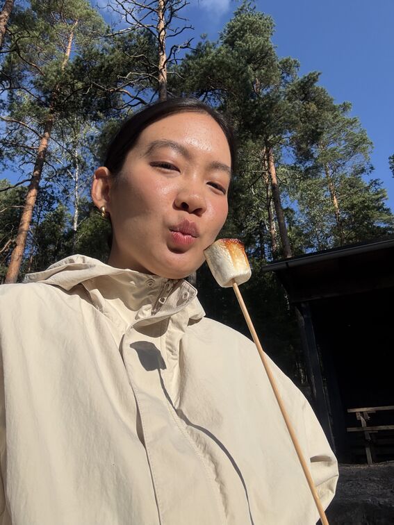 Person in a light jacket holding a toasted marshmallow on a stick in a sunny forest