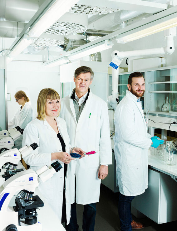 Four scientists in white lab coats stand in bright lab, microscopes and equipment visible around them