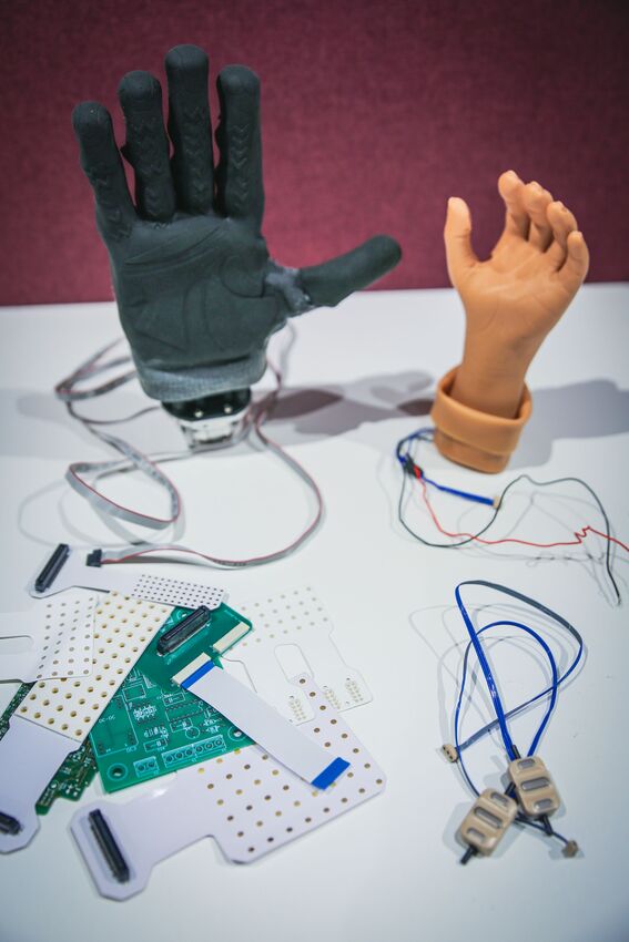 Robotic and prosthetic hands on a table with circuit boards, cables and connectors for testing