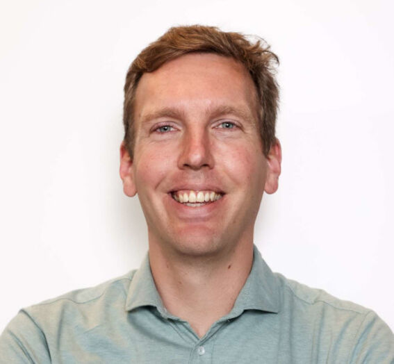 Smiling adult man with short light brown hair in a pale green shirt against a plain light background