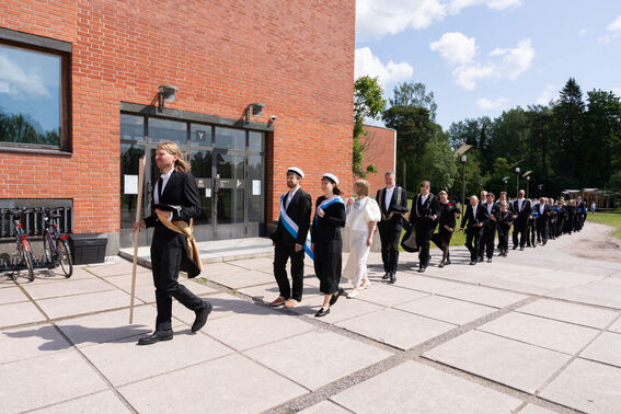 People walking in a procession next to a red brick building.