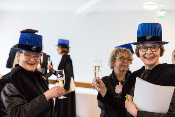 People in academic gowns and blue hats holding champagne glasses.