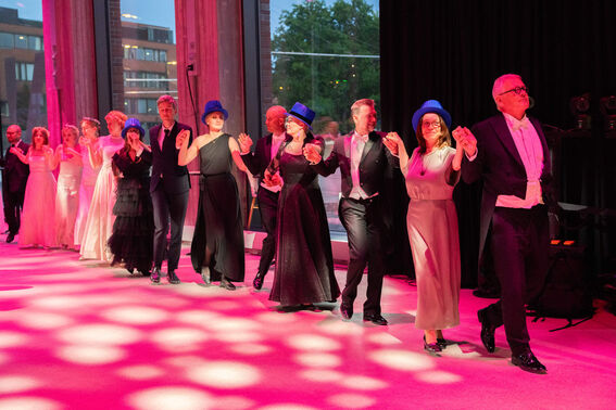 A group of formally dressed people dancing indoors under bright pink lights.