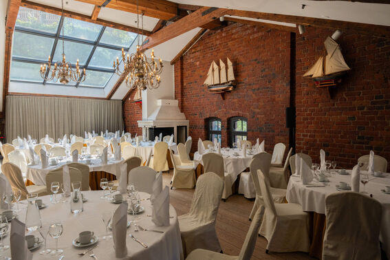 A restaurant with round tables set for dining, brick walls, chandeliers, and model ships on display.