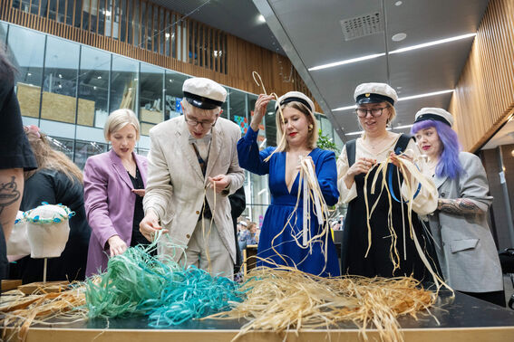 Group of people wearing graduation caps, dressing hats with colourful ribbons in a modern building.