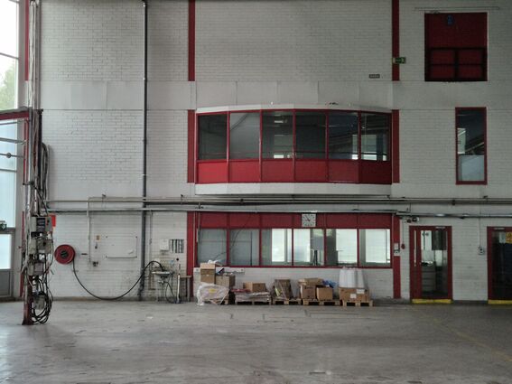 Industrial warehouse interior with white walls and red-framed windows and doors. Boxes and equipment on the floor.
