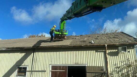 A worker in safety gear on an old tiled roof under a blue sky.