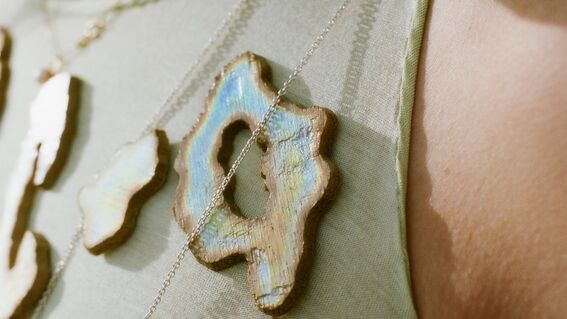 Close-up of a person wearing necklaces with iridescent wooden pendants on a light green fabric.