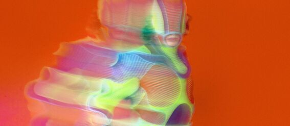 A blurred figure in a colourful, futuristic outfit against an orange background.