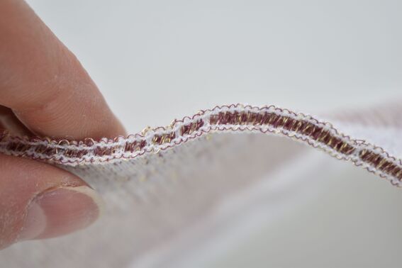 Close-up of a hand holding a piece of fabric with detailed stitching along the edge.