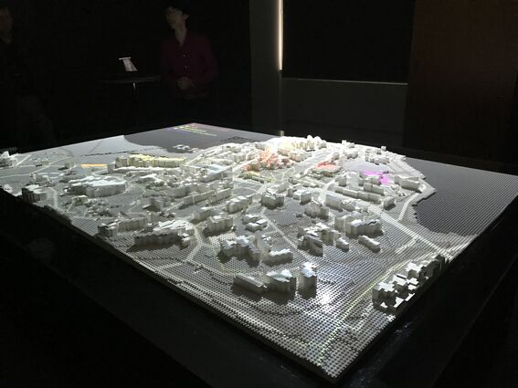 A detailed architectural model of a city displayed on a table in a dimly lit room.