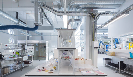 A modern laboratory with equipment, shelves, and tables. Ventilation ducts are visible on the ceiling.