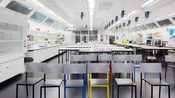 A modern laboratory with workstations and colourful chairs. Shelves with equipment line the walls. Large windows provide natural light.