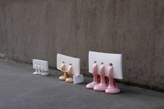 Three abstract sculptures with different shapes and colours are placed against a concrete wall.