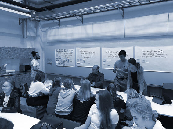 A group of people in a classroom discussing ideas written on large papers on the wall.