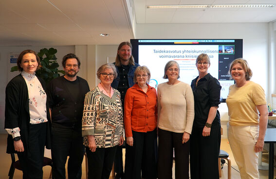 Group of adults posing indoors in front of a large presentation screen 