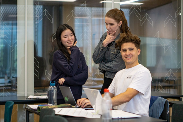 Three students posing with laptops and study material.