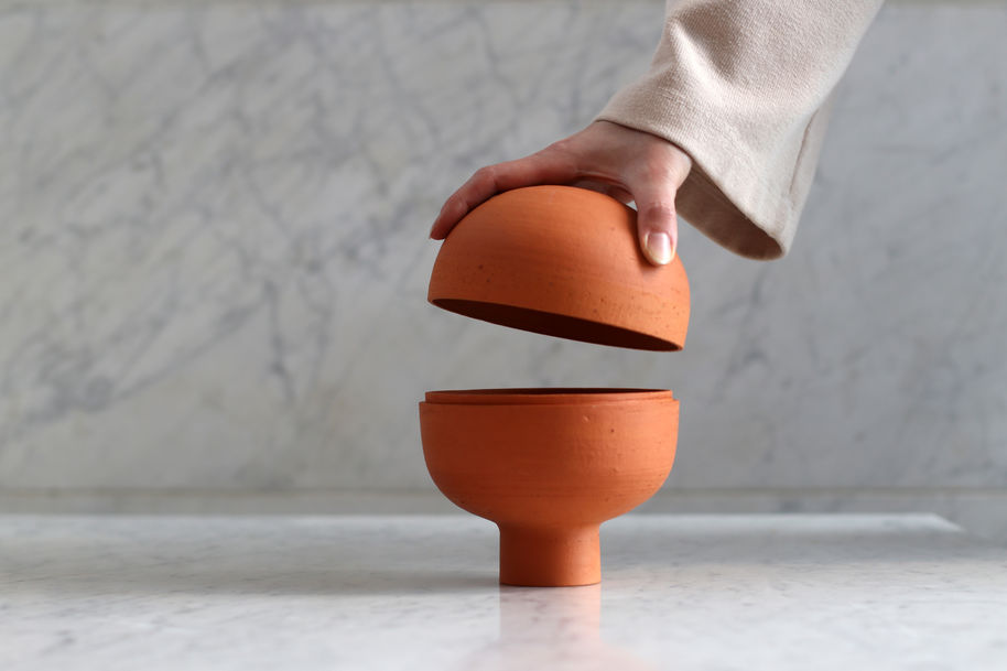a ceramic 2 piece container and a hand lifting the lid of it
