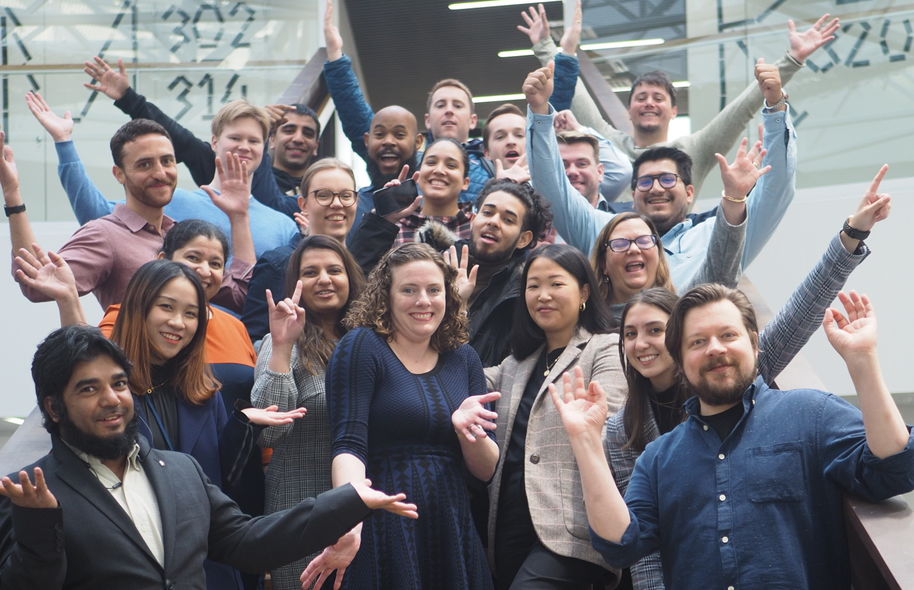 Group pucture taken at the stairs in Väre of happy Digital Business students, smiling and waving to the camera.