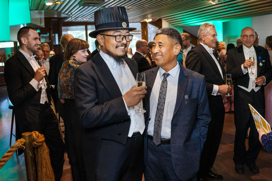 Frakkeihin ja juhlapukuihin sonnustautuneet ihmiset hymyilevät kuohuviinilasit käsissään