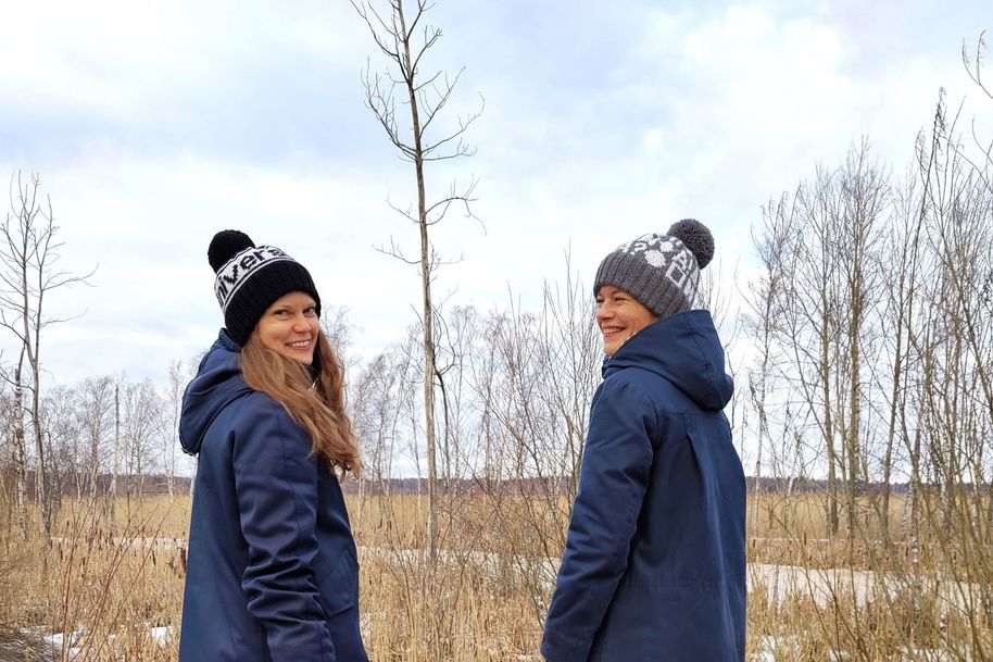 Kaksi naista seisoo hymyillen merimaiseman edessä.