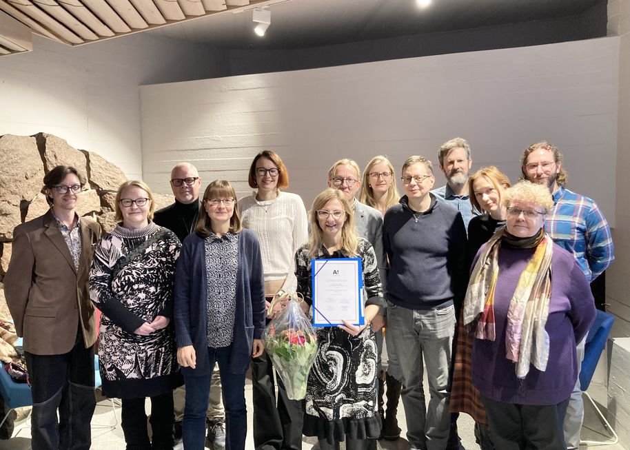 Ryhmä ihmisiä seisoo sisällä, yhdellä on todistus ja kukkakimppu.