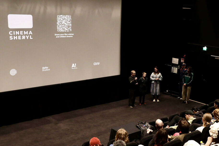 A group of people standing on a stage in a cinema, with an audience seated in front of them.