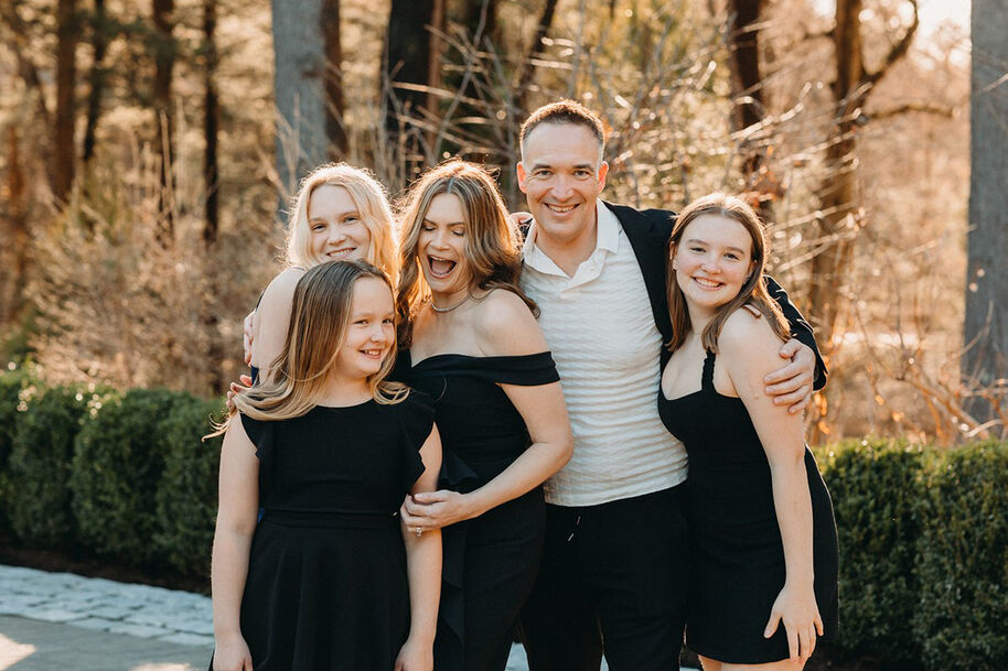 Perhekuva ulkona, jossa viisi mustiin pukeutunutta ihmistä. Taustalla näkyy puita ja pensaita.