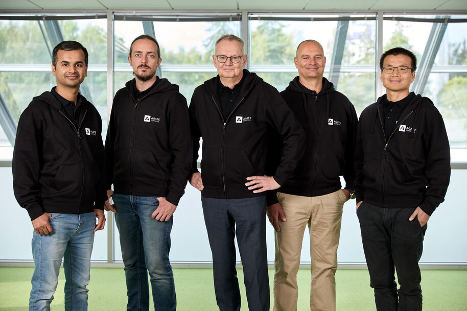Five men in black hoodies with company logos stand indoors, with windows in the background.
