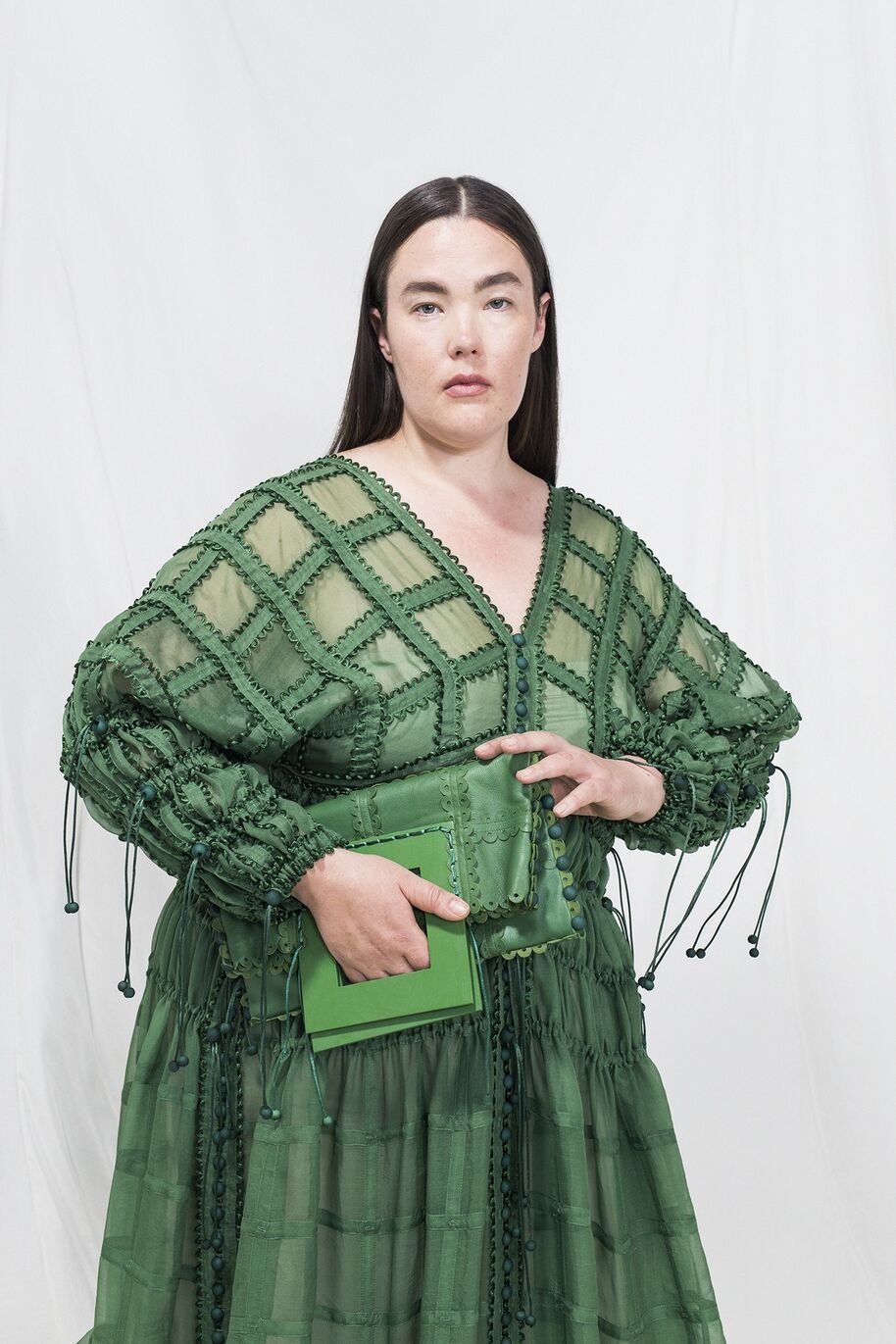 Henkilö pukeutuneena vihreään mekkoon, jossa on yksityiskohtaisia kuvioita, pitää vihreää laukku.