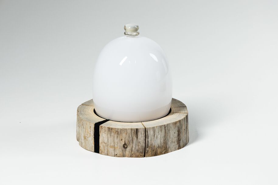 A white glass dome with a knob on top, placed on a circular wooden base with visible cracks.