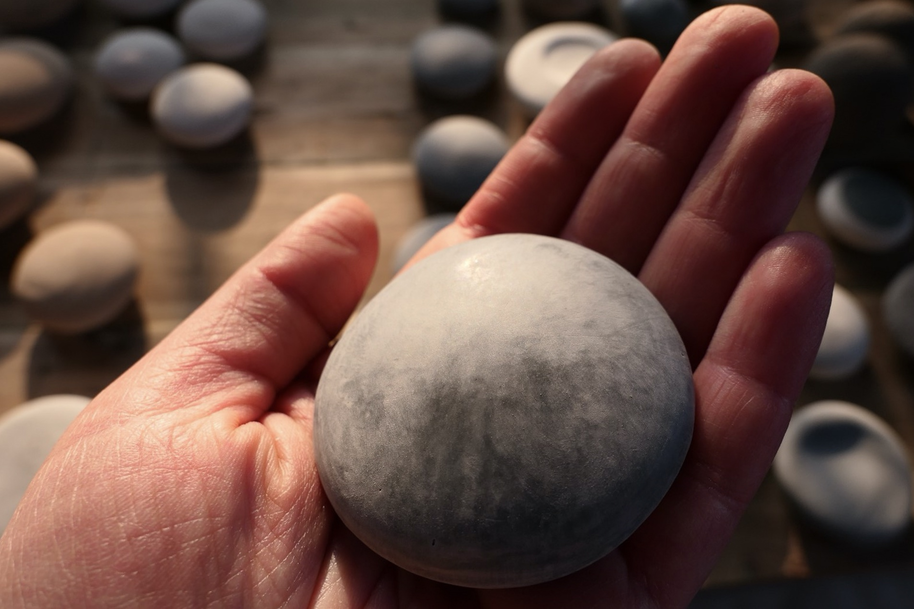 A hand holding a smooth, round stone. Several similar stones are scattered on a wooden surface in the background.
