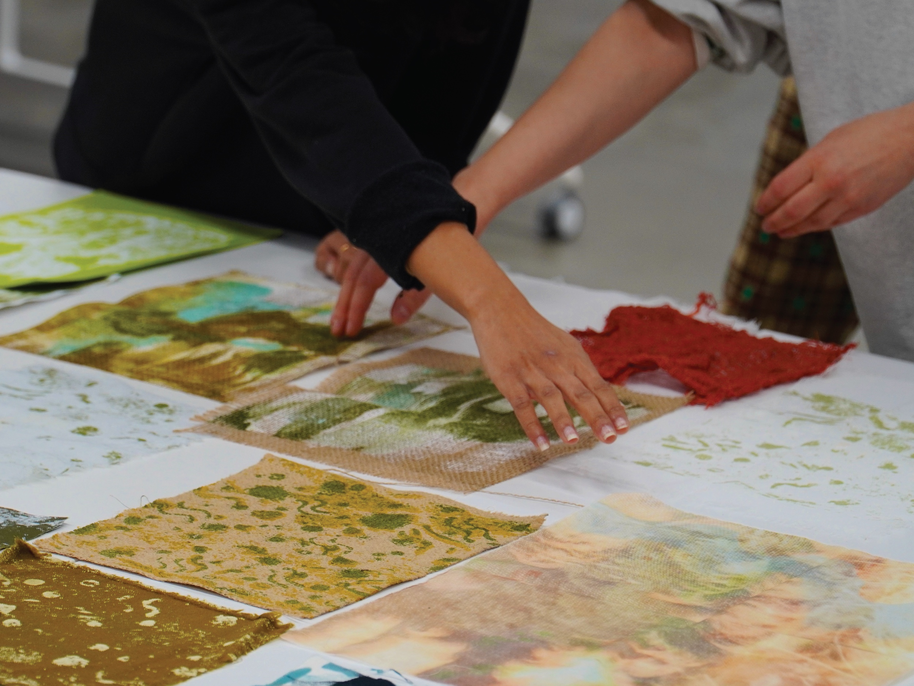 Two people arranging various textured and coloured fabric samples on a white table.