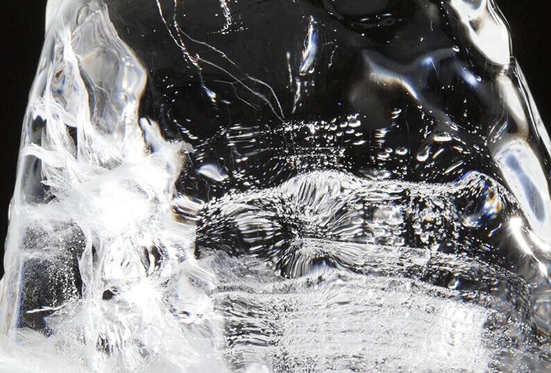 Close-up of a clear ice block with intricate patterns and bubbles inside, against a dark background.