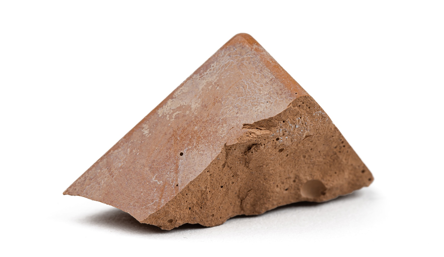 A triangular piece of brown rock with a rough texture on one side and a smooth surface on the other, placed on a white background.