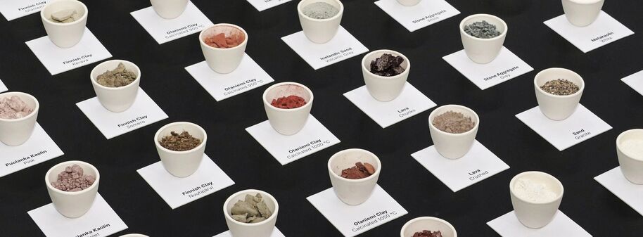 Small cups filled with various coloured clays on a black surface, each labelled with its type and origin.