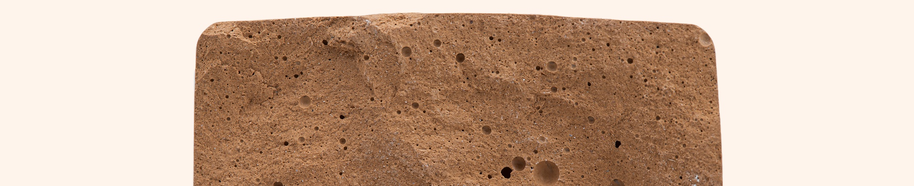 Close-up of a brown porous brick with various sized holes and rough texture against a light beige background.