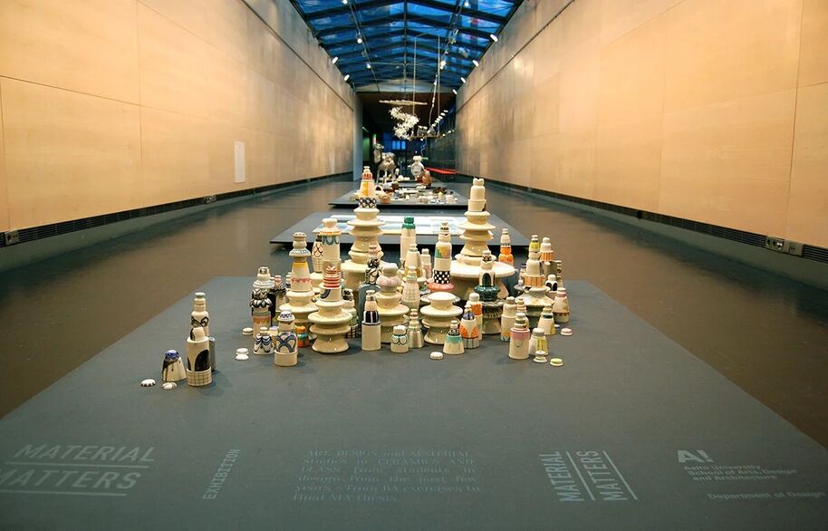 An exhibition hall with various stacked ceramic pieces on display tables. The ceiling is made of glass panels.