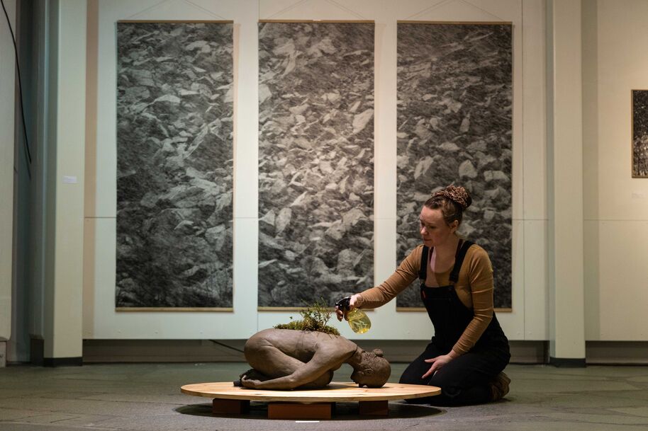 Mira Niittymäki waters her installation made from clay gathered from Utsjoki, on the back Vertti Virasjoki’s photograph from Deatnu bank. Photo: Vertti Virasjoki.