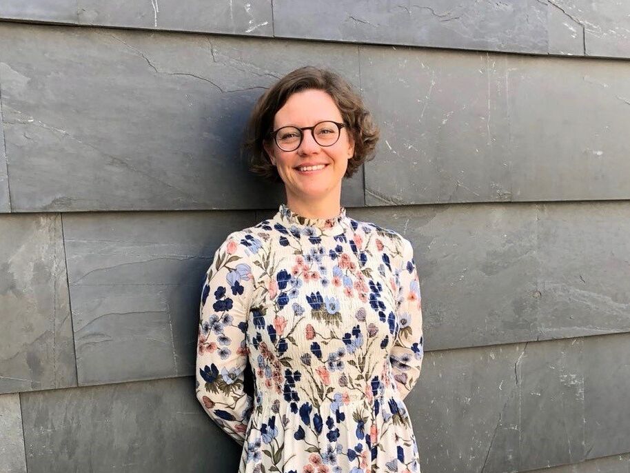 Henkilö seisoo harmaata kiviseinää vasten, yllään kukkamekko, jossa on sinisiä, vaaleanpunaisia ja vihreitä kuvioita.