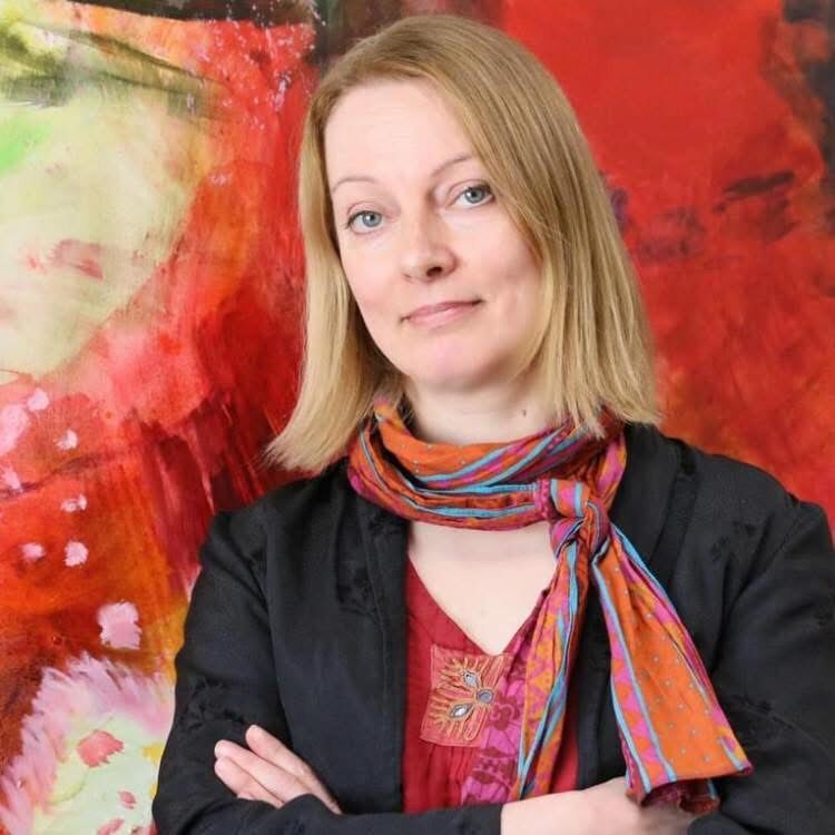 Henkilö ristissä käsin, värikäs huivi ja musta takki, seisoo eläväisen abstraktin maalauksen edessä.