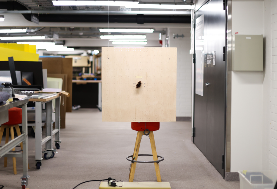 Large pale wooden board on a tripod with drilled centre, in a bright workshop hallway