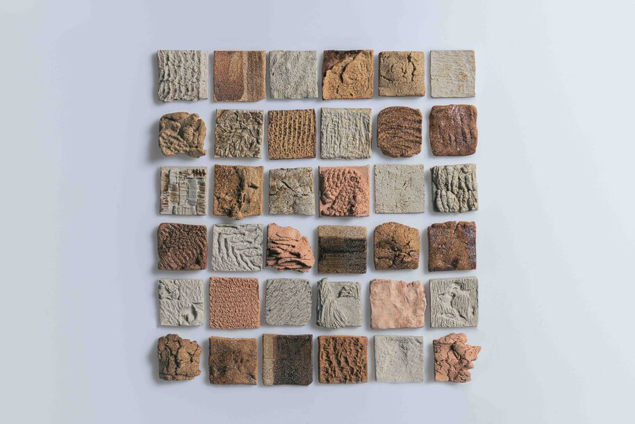 Square grid of small textured clay tiles in brown and grey tones on a light background