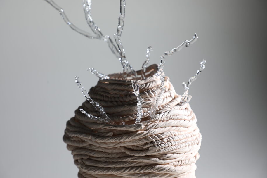 Coiled beige rope sculpture with twisted silver wire branches rising from the top, on a grey background.